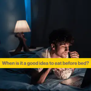 White man lying on his front on a bed watching a laptop. He's eating a bowl of popcorn. Words When is it a good idea to eat before bed