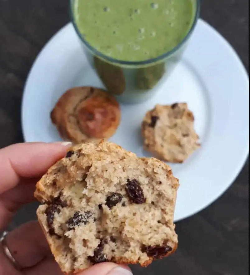 Close up of a broken breakfast muffin, in the background on a white plate is some pieces of muffin and a green smoothie