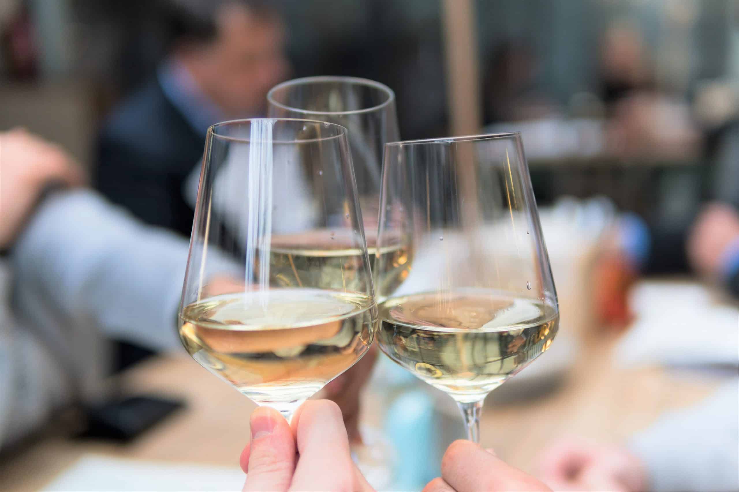 close up of 3 glasses of white wine, with blured background of busy cafe