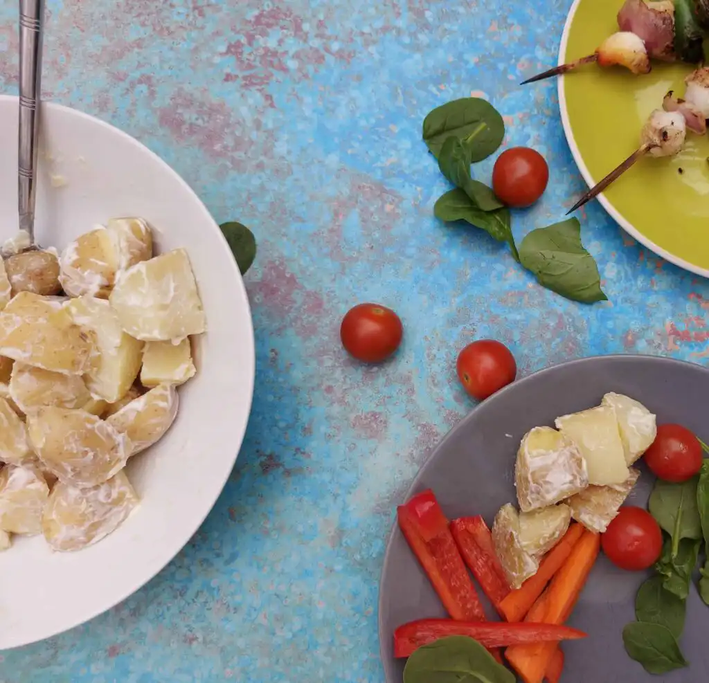 potato salad blue background- benefits gut health - goodness me nutrition potato salad and chopped red peppers, BBQ skewers against a blue background