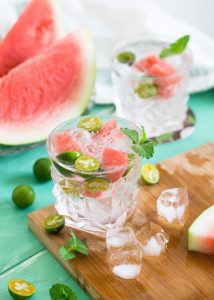 slices of watermelon, glass of water with ice and mint on a wooden board