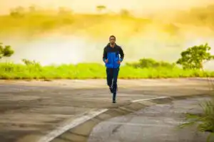 man running on a road, wearing a blue tracksuit, yellow sunlight behind him