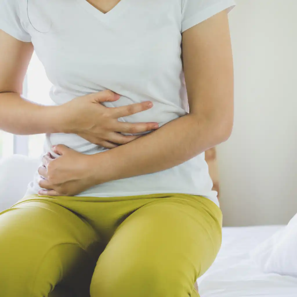 woman in white T shirt and green trousers holding stomach.