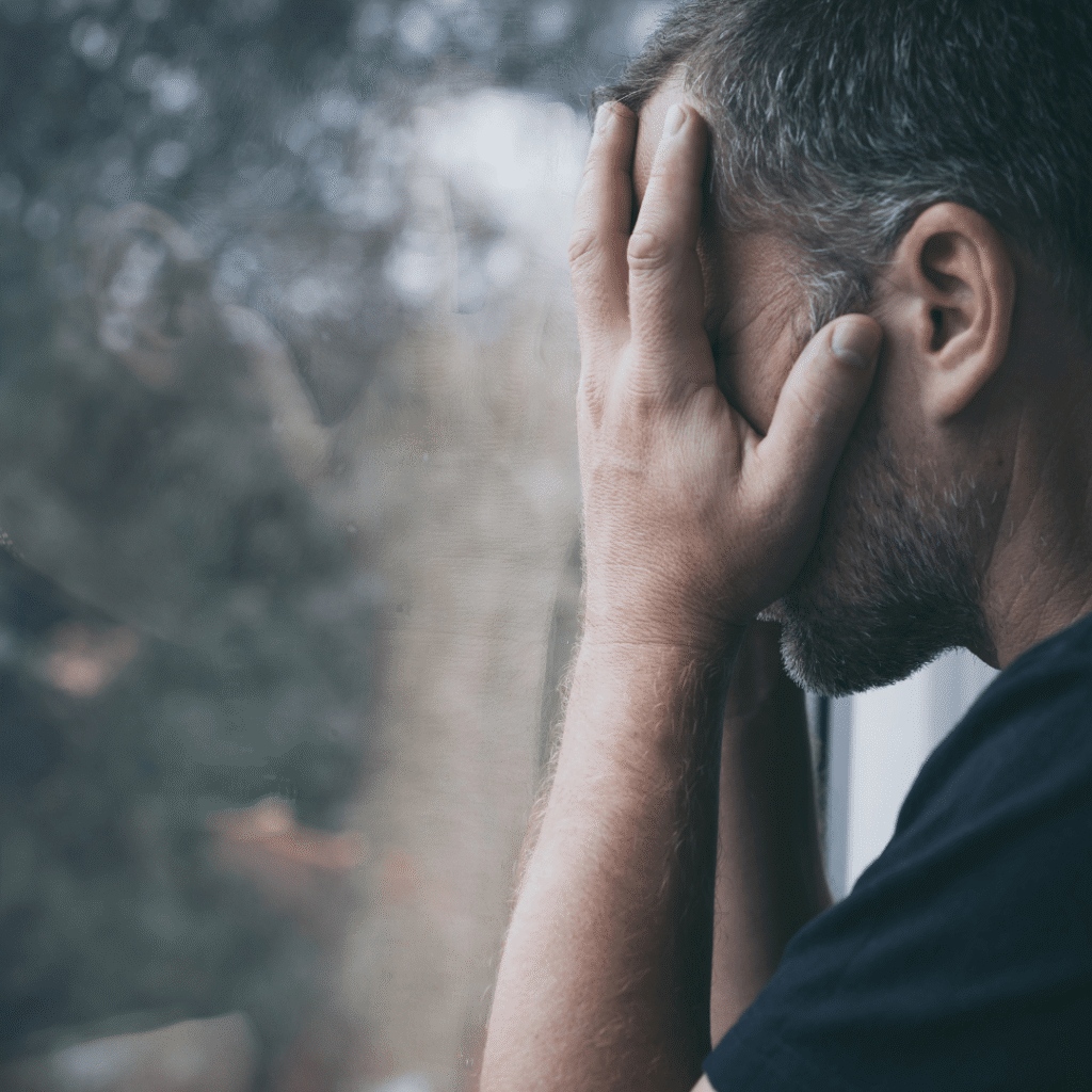 9 causes of fatigue in IBS 1 man holding head in hands next to a window, feeling fatigue in IBS