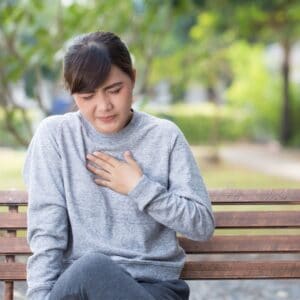 asian-woman-in-grey-sitting-on-bench-holding-hand-against-chest-closed-eyes-acid-reflux-foods