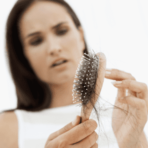 white woman in white vest looking at a hair brush with loose hairs
