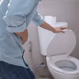 white man in blue shirt reaching for an open toilet seat, clutching his stomach