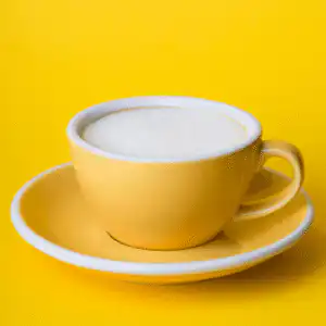 yellow cup and saucer against yellow background, frothy coffee in cuo