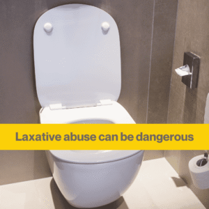 A white toilet in a grey bathroom. A yellow banner with the words Laxative abuse can be dangerous.