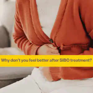 SIBO treatment didn't work (1) Woman's torso close up. She is wearing an amber cardigan and white T shirt, white trousers. She is clutching her stomach. The words Why you don't feel better after SIBO treatment.