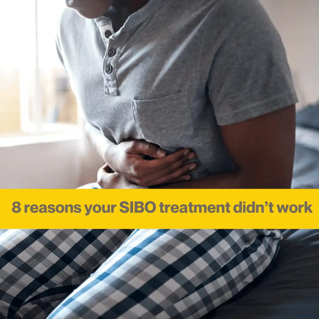 Person with dark skin sitting on a bed wearing blue & white checked pajama bottoms and a grey t shirt. They are clutching their stomach as if in pain. The words 8 reasons your SIBO treatment didn't work.