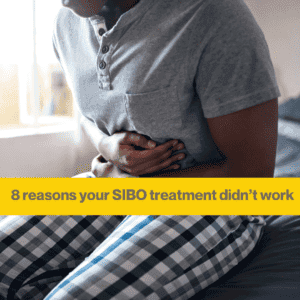 Person with dark skin sitting on a bed wearing blue & white checked pajama bottoms and a grey t shirt. They are clutching their stomach as if in pain. The words 8 reasons your SIBO treatment didn't work. 