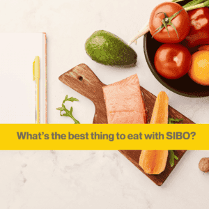 white kitchen surface with a wooden board and two pieces of raw salmon, a bowl with a tomato and an avocado.