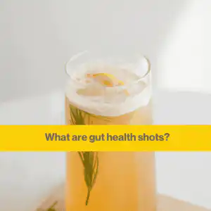 gut health shots - nutritionist (1) Glass containing some orangey yellow liquid and a sprig of rosemary. The background is a white wall with sunlight in the coner.
