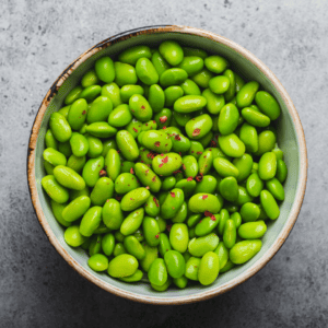 Bowl of cooked edamame beans against a pale blue stone background. 