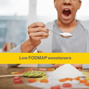 which sweeteners are low FODMAP - goodness me nutrition (1) Close up of a man's hand holding a teaspoon of white sugar over a pile of white sugar on a table, with some sweets amongst the sugar.