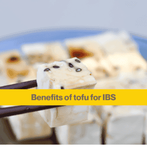 close up of a square of white tofu in black chopsticks, in the blurred background are more squares of tofu. 