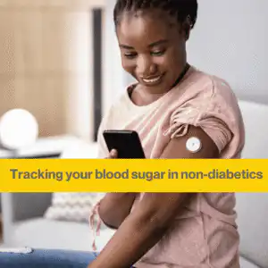 black woman sitting on a sofa looking at her phone. She has a white continuous glucose monitor in her arm and is smiling at her phone.