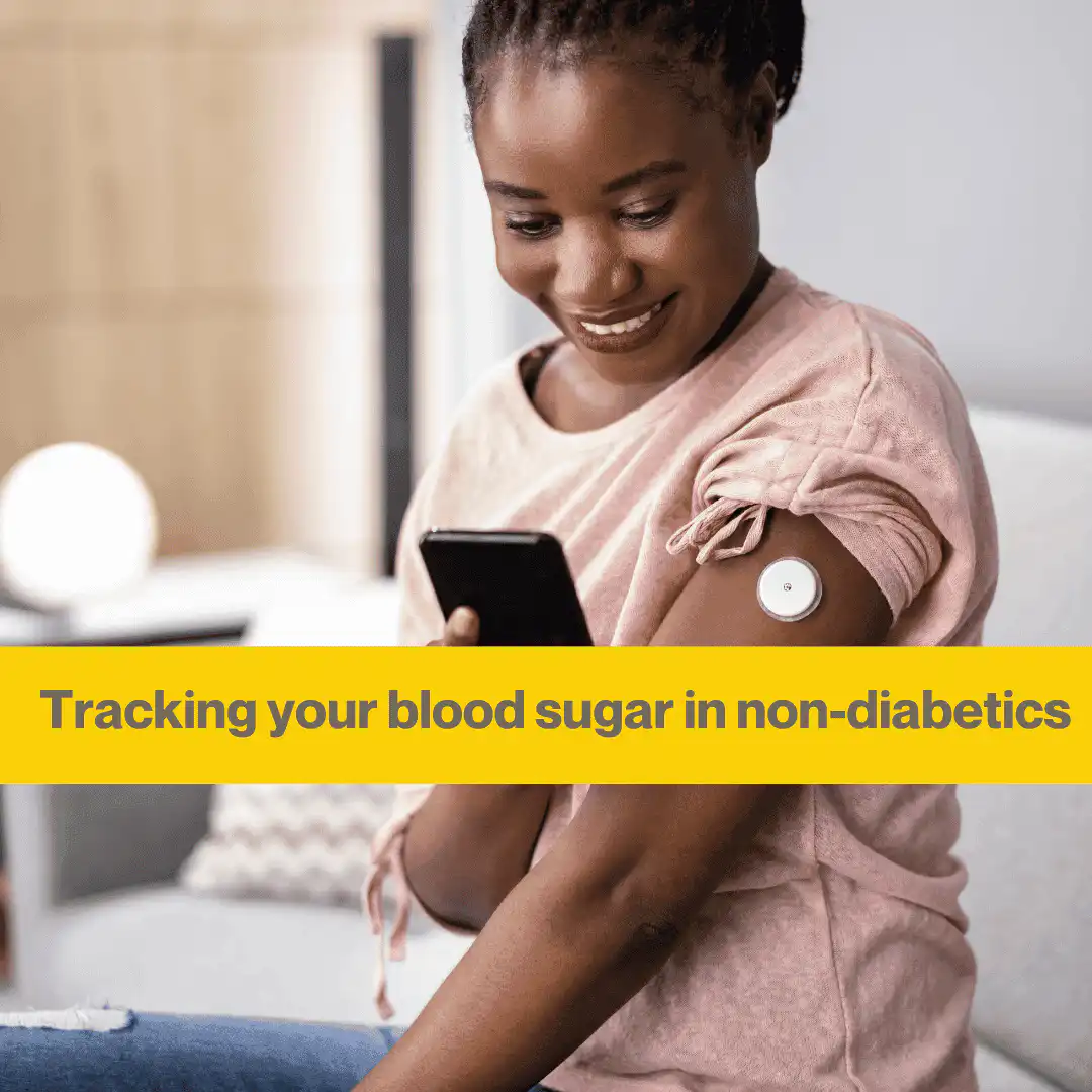 black woman sitting on a sofa looking at her phone. She has a white continuous glucose monitor in her arm and is smiling at her phone.