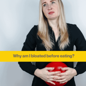 Woman with long blond hair in a black shirt holding a squishy red ball to her stomach, she looks in pain.