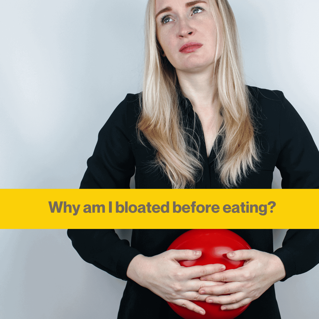 Woman with long blond hair in a black shirt holding a squishy red ball to her stomach, she looks in pain.