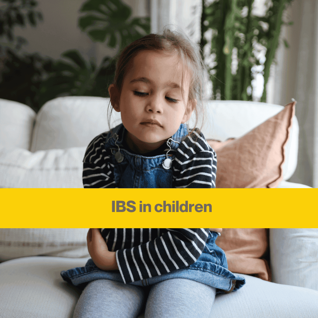 Small girl sitting on a sofa holding her stomach, eyes closed.