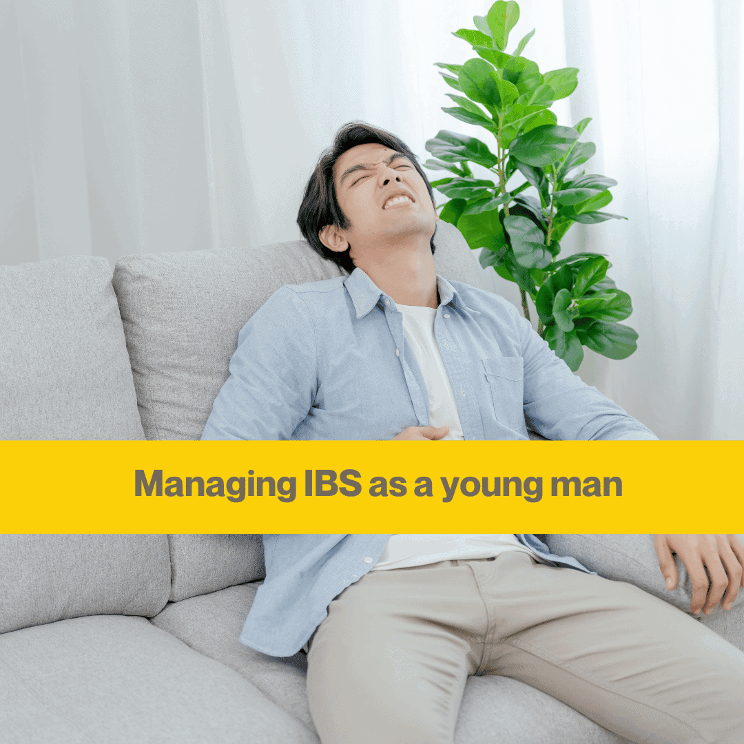 Man sits on a beige couch leaning back holding his stomach. He is wearing a light blue shirt, white t shirt and beige trousers. Words Managing IBS as a young man
