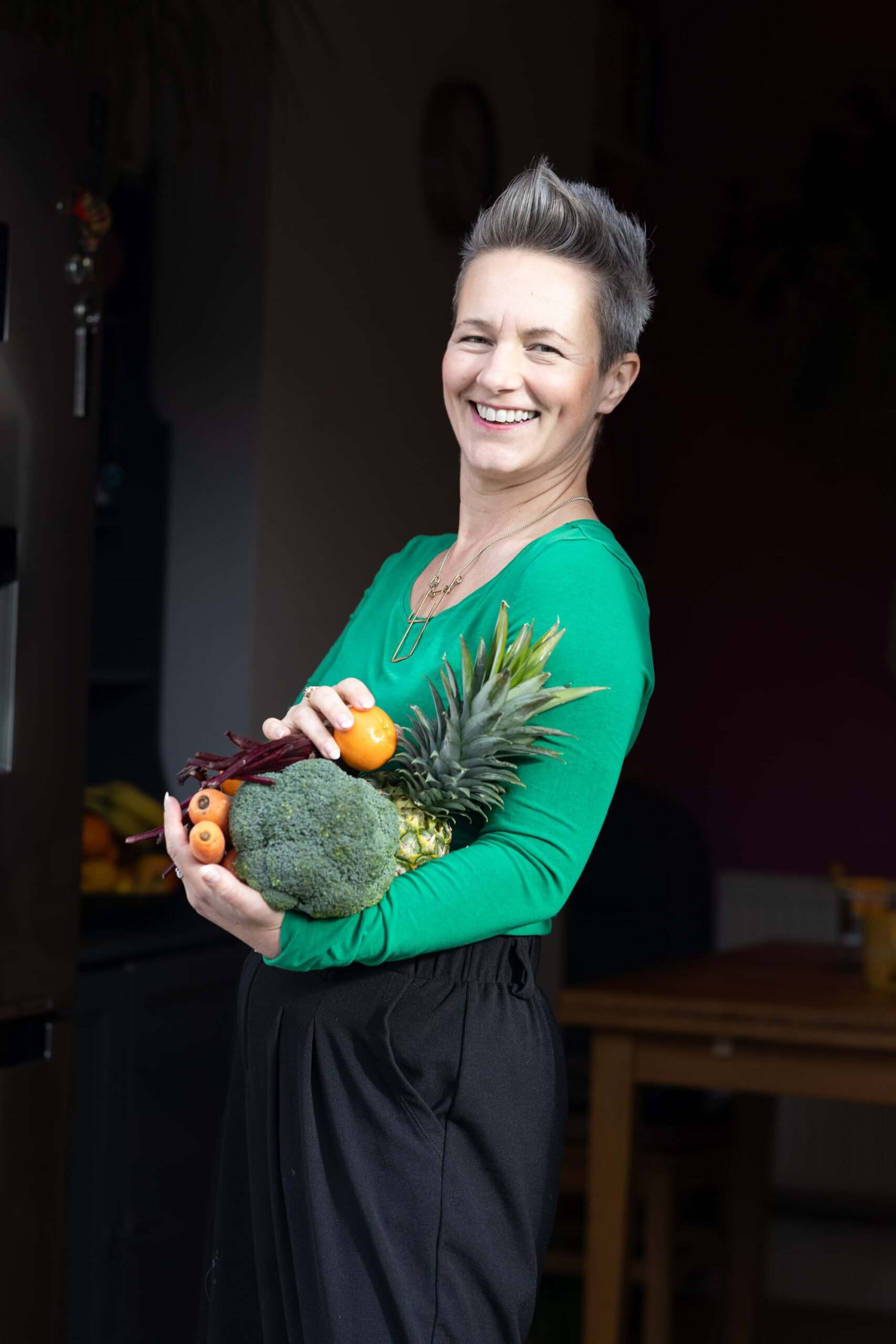 Close up of Anna Mapson holding pineapple, broccoli, oranges, carrots and beetroot. IBS friendly food
