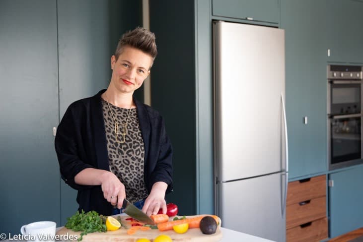 Nutritionist reviewing a meal plan with a man seated at a table, with fruits, a clipboard, and healthy food items visible in a bright kitchen setting.