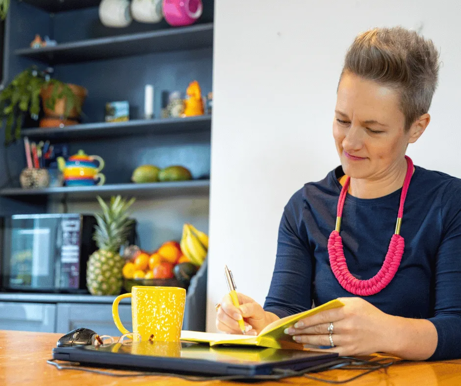 Nutritionist reviewing a meal plan with a man seated at a table, with fruits, a clipboard, and healthy food items visible in a bright kitchen setting.