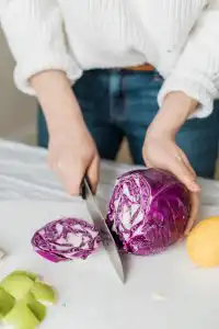 Nutritionist reviewing a meal plan with a man seated at a table, with fruits, a clipboard, and healthy food items visible in a bright kitchen setting.