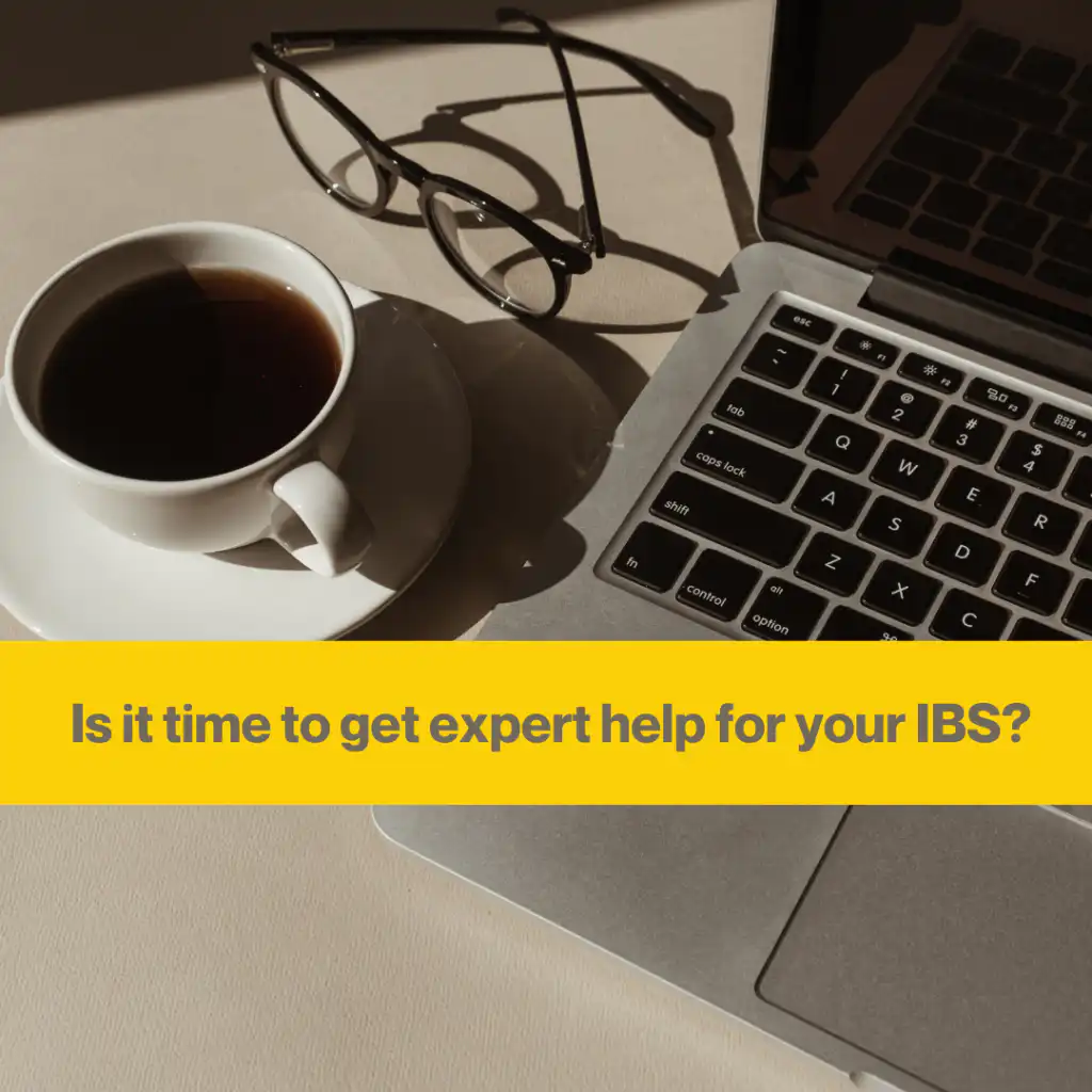 Grey laptop and a white coffee cup next to it. Glasses on the table creating a shadow in the sunlight. Words Is it time to get expert help for your IBS